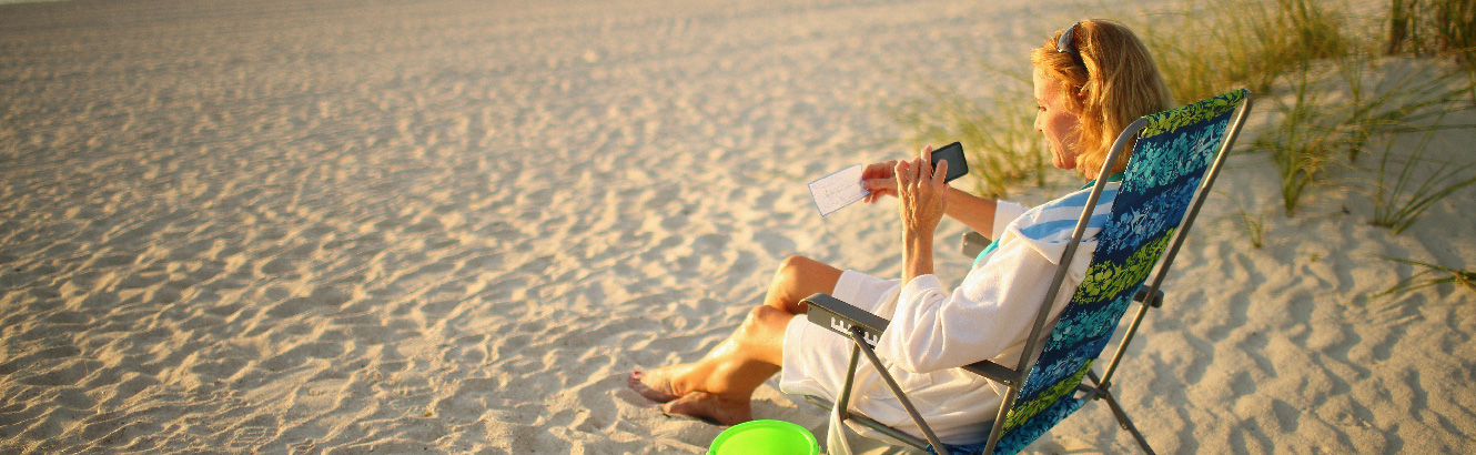 woman on beach using phone to deposit check